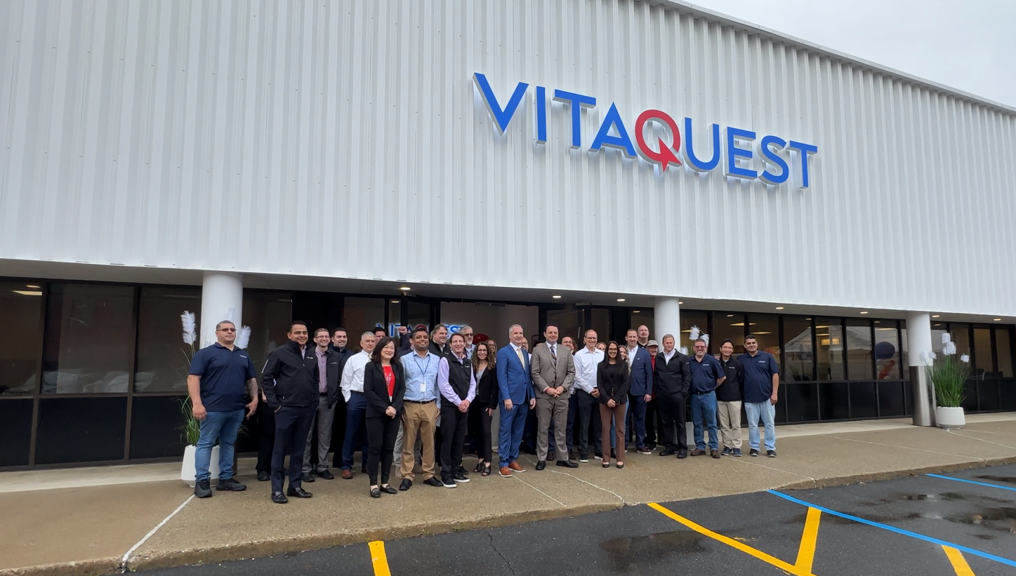 Exterior of Vitaquest's new Paterson facility. Vitaquest Staff with CEO Patrick Brueggman and Paterson Mayor Andre Sayegh at center. Image courtesy of Vitaquest.
