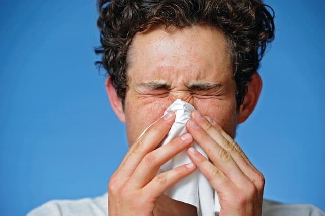 man blowing his nose on blue background